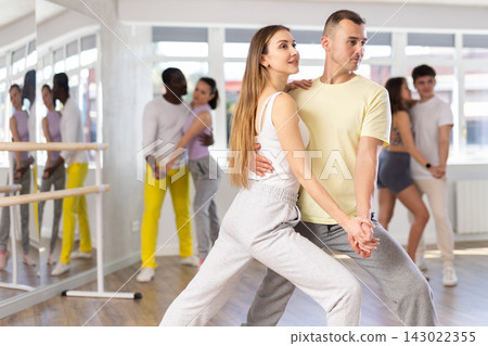 Smiling young woman and man in sportswear learn to dance couples latin dance, energetic and fast tango in dance salon Smiling young woman and man in sportswear learn to dance couples latin dance, energetic and fast tango in dance salon 143022355