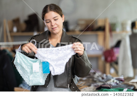 Young pretty woman shopper examining and choosing white panties in underwear shop Young pretty woman shopper examining and choosing white panties in underwear shop 143022382