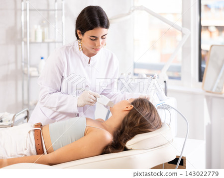 Female cosmetologist performing facial skin cleansing with ultrasonic shovel on woman Female cosmetologist performing facial skin cleansing with ultrasonic shovel on woman 143022779