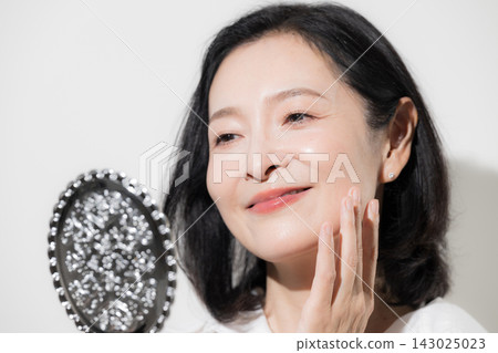 【白色背景】一位五十多歲的日本女性正在鏡子前檢查臉頰上的肌膚。美麗的肌膚,護膚,抗衰老護理,緊緻和光澤。 【白色背景】一位五十多歲的日本女性正在鏡子前檢查臉頰上的肌膚。美麗的肌膚,護膚,抗衰老護理,緊緻和光澤。 143025023