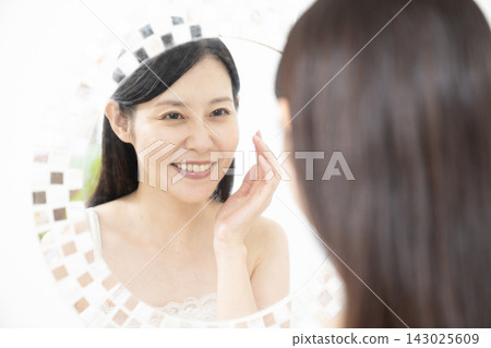 一位女士在做了睫毛嫁接後對著鏡子微笑。 一位女士在做了睫毛嫁接後對著鏡子微笑。 143025609