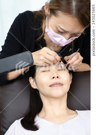 Woman receiving eyelash extension treatment Woman receiving eyelash extension treatment 143025665