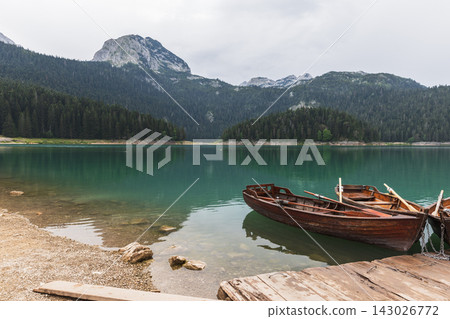 Wooden rowboats tied to a small dock on a tranquil mountain lake, Montenegro Wooden rowboats tied to a small dock on a tranquil mountain lake, Montenegro 143026772