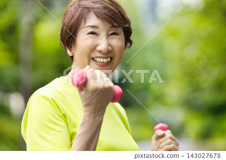 一位微笑的老婦人手持粉紅色啞鈴。 一位微笑的老婦人手持粉紅色啞鈴。 143027678