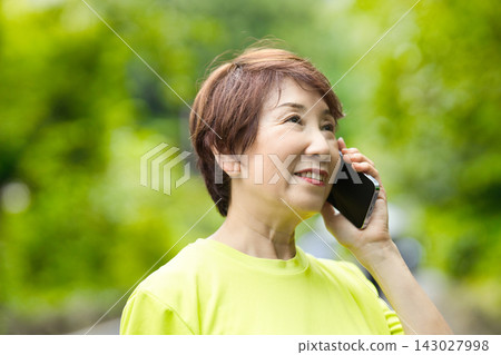 一位身穿運動服的老婦人正在用智慧型手機通話 一位身穿運動服的老婦人正在用智慧型手機通話 143027998