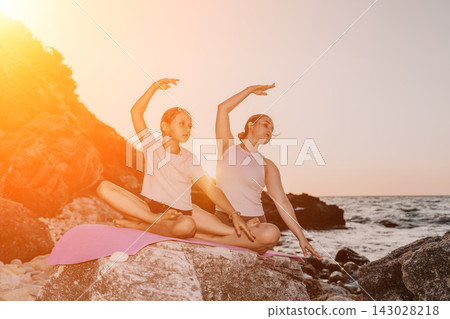 Serene yoga practice by mother and daughter on coastal rocks during sunset Serene yoga practice by mother and daughter on coastal rocks during sunset 143028218