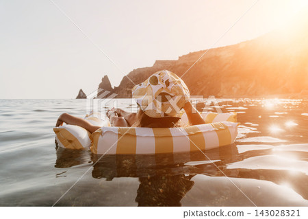 Woman, Inflatable, Beach: A woman relaxes on a striped inflatable raft in the ocean, with rocky cliffs in the background. Woman, Inflatable, Beach: A woman relaxes on a striped inflatable raft in the ocean, with rocky cliffs in the background. 143028321