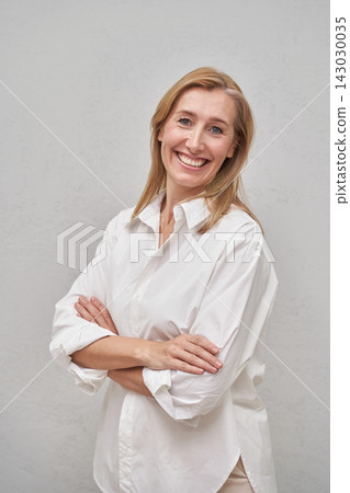 Blonde Woman Standing With Arms Crossed And Smiling In White Shirt Against Plain Gray Studio Blonde Woman Standing With Arms Crossed And Smiling In White Shirt Against Plain Gray Studio 143030035