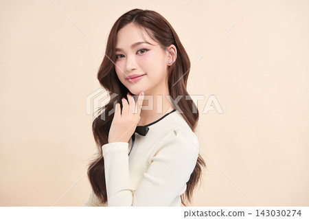 A beautiful young Asian woman with clean, fresh skin against a beige background. Skincare, facial treatment, cosmetology, beauty, and spa. An elegant portrait of an Asian woman. 143030274