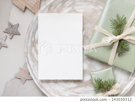 Christmas card mockup on wooden plate near sage green gift box and rustic decor top view Christmas card mockup on wooden plate near sage green gift box and rustic decor top view 143030312