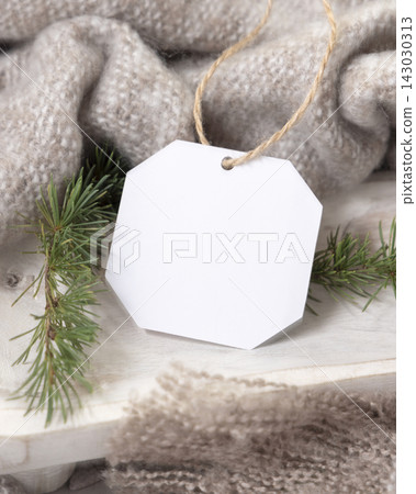 Blank gift tag mockup near beige knitted blanket and fir branches. Rustic Christmas packaging Blank gift tag mockup near beige knitted blanket and fir branches. Rustic Christmas packaging 143030313