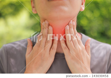 Close up of woman touching her sore throat with both hands, red highlighted area indicating severe pain, thyroid gland problems, inflammation, or tonsillitis symptom. Healthcare and medical concept. Close up of woman touching her sore throat with both hands, red highlighted area indicating severe pain, thyroid gland problems, inflammation, or tonsillitis symptom. Healthcare and medical concept. 143030458