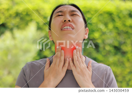 Close up of woman touching her sore throat with both hands, red highlighted area indicating severe pain, thyroid gland problems, inflammation, or tonsillitis symptom. Healthcare and medical concept. Close up of woman touching her sore throat with both hands, red highlighted area indicating severe pain, thyroid gland problems, inflammation, or tonsillitis symptom. Healthcare and medical concept. 143030459