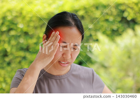 Unhappy young Asian woman touching head with red highlighted area indicating severe headache, migraine, or brain pain. Concept of stress, sickness, healthcare, tension and mental health problem. 143030460