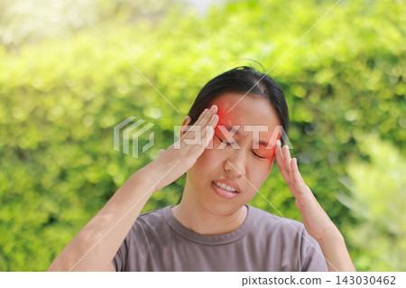 Unhappy young Asian woman touching head with both hands, red highlighted area indicating severe headache, migraine, or sinus pain. Concept of stress, sickness, healthcare, tension and mental problems. Unhappy young Asian woman touching head with both hands, red highlighted area indicating severe headache, migraine, or sinus pain. Concept of stress, sickness, healthcare, tension and mental problems. 143030462