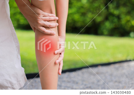 Close up of person grasping bare calf muscle with red highlighted area indicating severe leg pain, muscle cramp, strain, or sports injury. Healthcare, physical therapy, medical concept outdoors. Close up of person grasping bare calf muscle with red highlighted area indicating severe leg pain, muscle cramp, strain, or sports injury. Healthcare, physical therapy, medical concept outdoors. 143030480