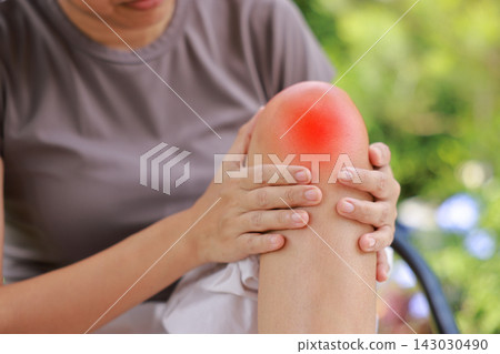 Close up of person sitting holding bare knee with red highlighted area indicating severe joint pain, arthritis, muscle ache or sports injury. Healthcare, physical therapy, medical orthopedic concept. Close up of person sitting holding bare knee with red highlighted area indicating severe joint pain, arthritis, muscle ache or sports injury. Healthcare, physical therapy, medical orthopedic concept. 143030490