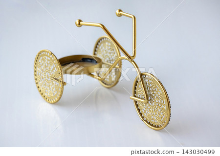 Decorative golden metal rickshaw tricycle tea light stand with intricate cut out wheels placed on plain white surface, elegant interior decor. Decorative golden metal rickshaw tricycle tea light stand with intricate cut out wheels placed on plain white surface, elegant interior decor. 143030499