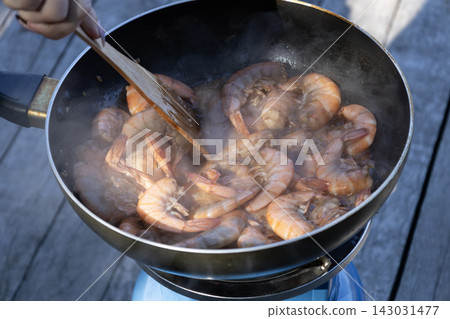 Delicious fresh shrimp frying with spices in a black pan outdoors being stirred with a wooden spatula Delicious fresh shrimp frying with spices in a black pan outdoors being stirred with a wooden spatula 143031477