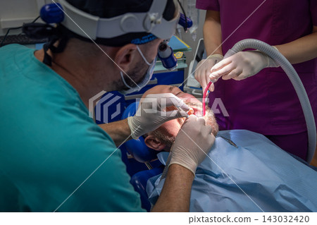 Dentist and assistant use a handpiece and suction during patient treatment Dentist and assistant use a handpiece and suction during patient treatment 143032420