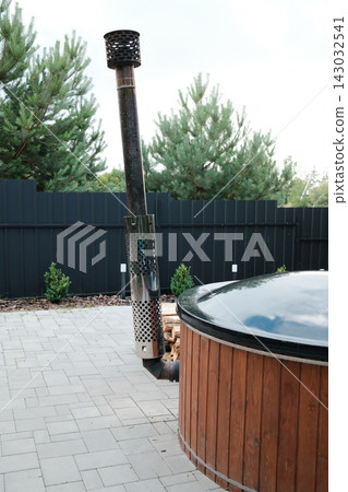 Wooden hot tub with a metal chimney standing on a patio during the day Wooden hot tub with a metal chimney standing on a patio during the day 143032541