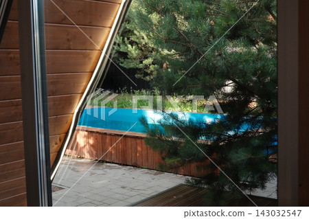 View from inside a wooden house toward a blue pool in a garden during daytime 143032547