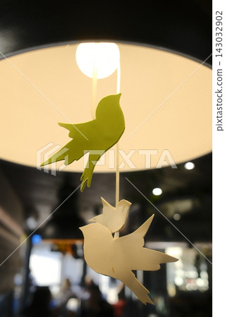 Decorative bird ornaments hanging from a bright lamp in a cafe Decorative bird ornaments hanging from a bright lamp in a cafe 143032902