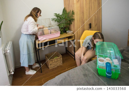 Two people are cleaning a hamster cage. One person is sitting Two people are cleaning a hamster cage. One person is sitting 143033568