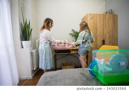 Two people are cleaning a hamster cage. One person is sitting Two people are cleaning a hamster cage. One person is sitting 143033569