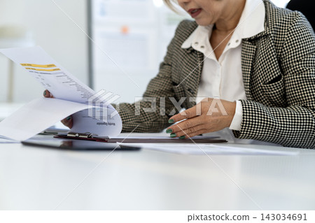 Senior Asian Businesswoman Reviewing Monthly Organization Documents at Modern Office Desk Senior Asian Businesswoman Reviewing Monthly Organization Documents at Modern Office Desk 143034691
