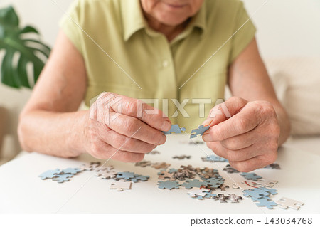 Senior woman's hands assembling puzzle pieces, engaging in mental exercise and brain training for dementia prevention Senior woman's hands assembling puzzle pieces, engaging in mental exercise and brain training for dementia prevention 143034768