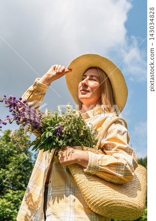 Woman in straw hat with basket of wildflowers including lupines and daisy enjoys sunny day outdoors. Rural lifestyle, flower picking, slow living and connection with nature Woman in straw hat with basket of wildflowers including lupines and daisy enjoys sunny day outdoors. Rural lifestyle, flower picking, slow living and connection with nature 143034828