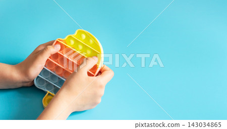 Fashionable touch bright toy antistress pop it in children's hands blue background copy space 143034865