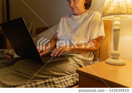 Caucasian adult female working on laptop in bed near lamp at night Caucasian adult female working on laptop in bed near lamp at night 143034959