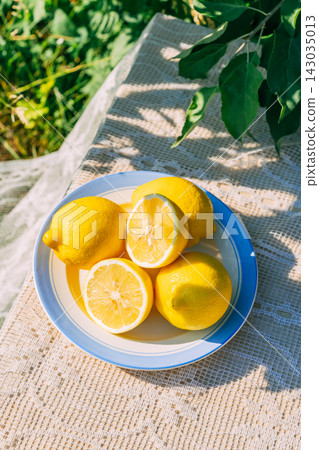 Fresh lemons in sunlight on a picnic table with green foliage Fresh lemons in sunlight on a picnic table with green foliage 143035013