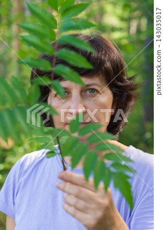 Mature caucasian female partially obscured by leaf in forest setting Mature caucasian female partially obscured by leaf in forest setting 143035017