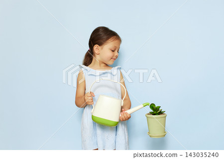 Young child holding a watering can, carefully watering a potted green plant against a light blue background Young child holding a watering can, carefully watering a potted green plant against a light blue background 143035240