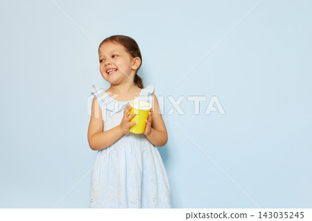 Little girl smiling, holding a yellow cup. Expressing childhood joy and happiness on a blue background 143035245
