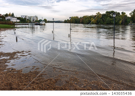 Flooded riverside promenade along Elbe in Magdeburg shows high water covering walkway and lamps near moored boat. Autumn landscape highlights flooding, weather, river level, infrastructure, and risk Flooded riverside promenade along Elbe in Magdeburg shows high water covering walkway and lamps near moored boat. Autumn landscape highlights flooding, weather, river level, infrastructure, and risk 143035436