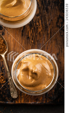 Creamy whipped Dalgona coffee dessert in glass jars on rustic wooden table with spoon and coffee grounds Creamy whipped Dalgona coffee dessert in glass jars on rustic wooden table with spoon and coffee grounds 143036539