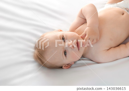 Happy naked baby in diaper lying on his back on the white sheet and touching his face. Baby girl with red hair looking at camera. Light background. Little child. Serious emotion. Advertising Mockup Happy naked baby in diaper lying on his back on the white sheet and touching his face. Baby girl with red hair looking at camera. Light background. Little child. Serious emotion. Advertising Mockup 143036615