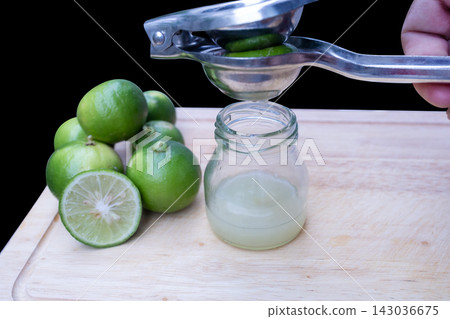View of Human hands squeezing fresh yellow lemon half over a glass, extracting citrus juice with splashing droplets, focus selective View of Human hands squeezing fresh yellow lemon half over a glass, extracting citrus juice with splashing droplets, focus selective 143036675