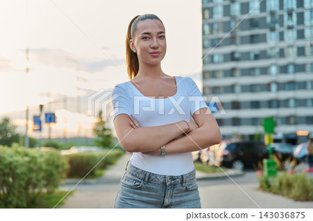 Confident young woman standing with arms crossed on city street outdoors Confident young woman standing with arms crossed on city street outdoors 143036875