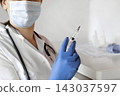Nurse pushing air out of syringe for vaccine injection. Doctor wearing blue gloves and medical mask. Person holds a syringe with medicine in his hand Close Up. She ready to give an injection. Science 143037597