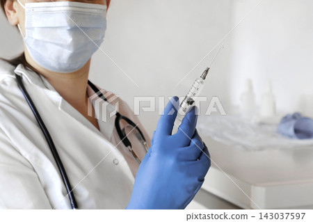 Nurse pushing air out of syringe for vaccine injection. Doctor wearing blue gloves and medical mask. Person holds a syringe with medicine in his hand Close Up. She ready to give an injection. Science Nurse pushing air out of syringe for vaccine injection. Doctor wearing blue gloves and medical mask. Person holds a syringe with medicine in his hand Close Up. She ready to give an injection. Science 143037597