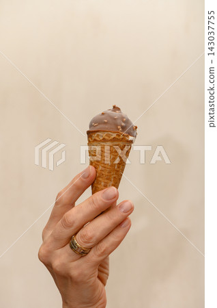 Close-up studio photograph of a hand holding a chocolate-dipped ice cream cone Close-up studio photograph of a hand holding a chocolate-dipped ice cream cone 143037755