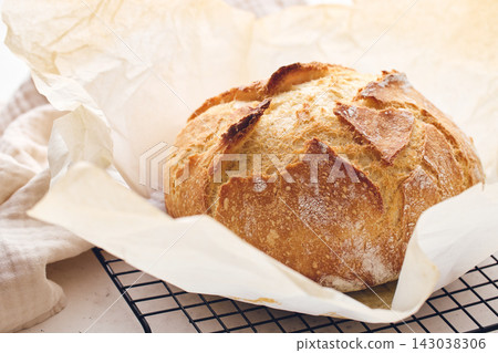 Round sourdough loaf resting on black wire cooling rack with beige linen towel. Perfect for baking, food blogs, and culinary projects Round sourdough loaf resting on black wire cooling rack with beige linen towel. Perfect for baking, food blogs, and culinary projects 143038306