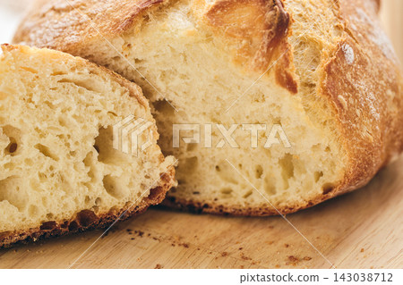 Sliced artisan sourdough bread with airy crumb on wooden board, glass of milk, and knitted cloth. Ideal for culinary, baking, and food photography projects. Sliced artisan sourdough bread with airy crumb on wooden board, glass of milk, and knitted cloth. Ideal for culinary, baking, and food photography projects. 143038712
