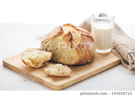 Sliced artisan sourdough bread with airy crumb on wooden board, glass of milk, and knitted cloth. Ideal for culinary, baking, and food photography projects. 143038713