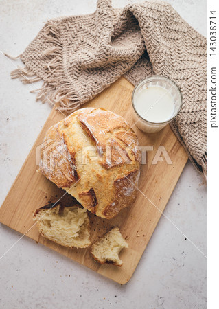 Sliced artisan sourdough bread with airy crumb on wooden board, glass of milk, and knitted cloth. Ideal for culinary, baking, and food photography projects. Sliced artisan sourdough bread with airy crumb on wooden board, glass of milk, and knitted cloth. Ideal for culinary, baking, and food photography projects. 143038714